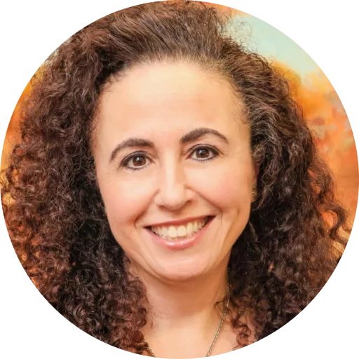 Woman with curly brown hair smiling at camera against warm orange background