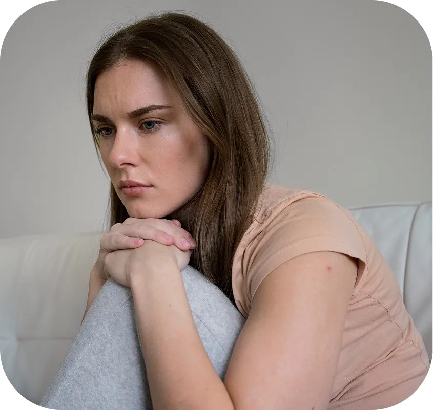 Woman with brown hair sitting on a couch, looking down with a concerned expression