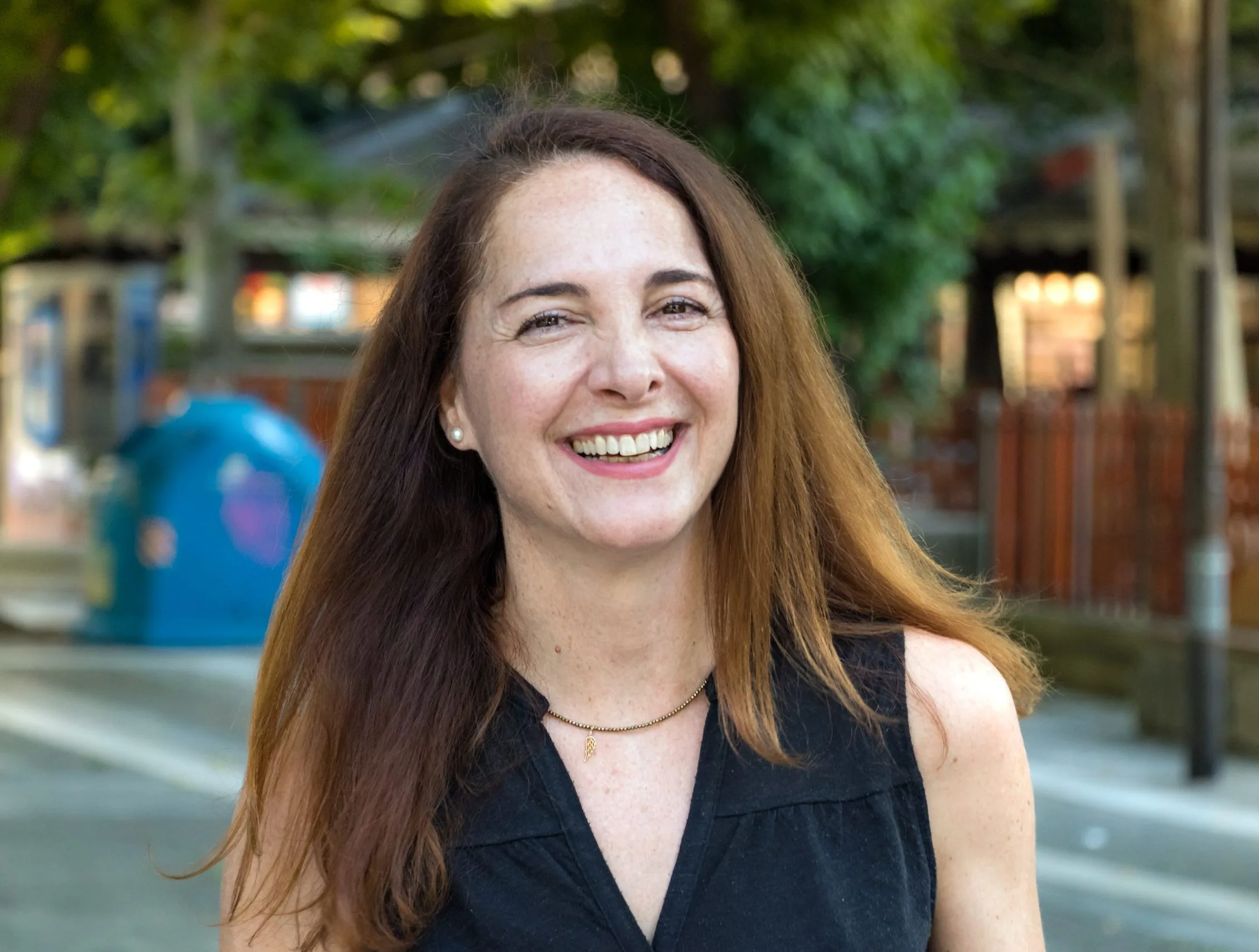 Smiling woman with long brown hair in an outdoor urban setting