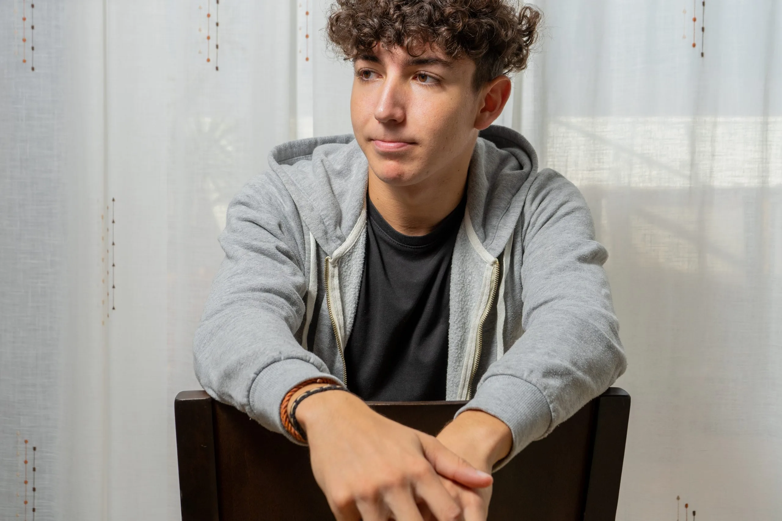 Young man in gray hoodie sitting pensively by a window