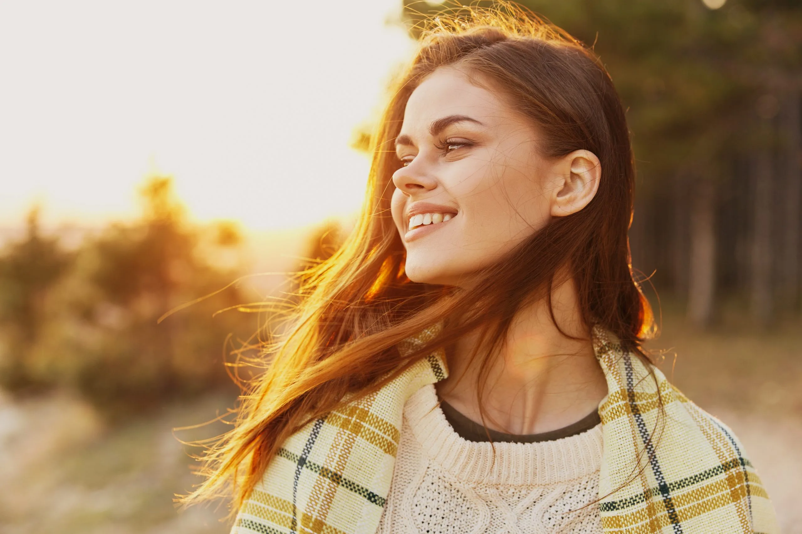 Woman with red hair smiling in golden sunlight wearing plaid cardigan
