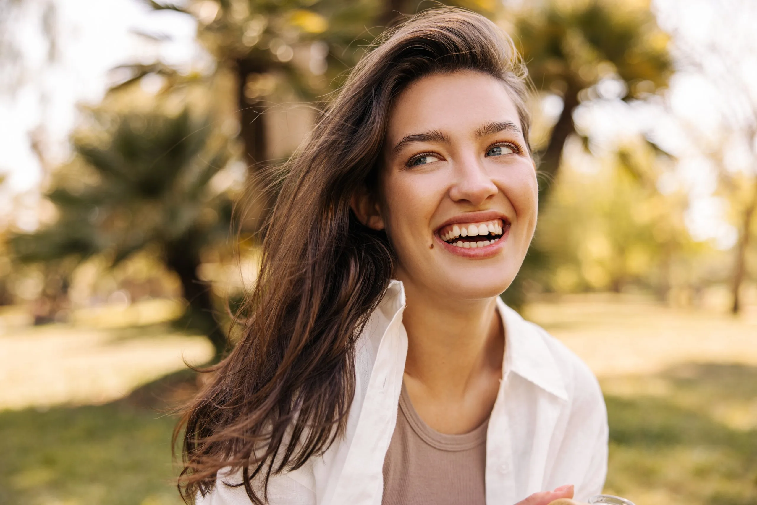 Woman laughing outdoors surrounded by green foliage and trees