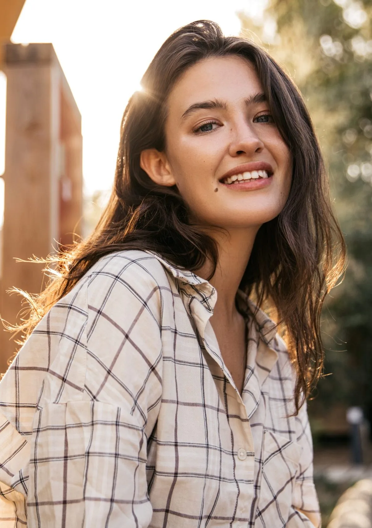 Woman in plaid shirt smiling while looking over shoulder in golden sunlight
