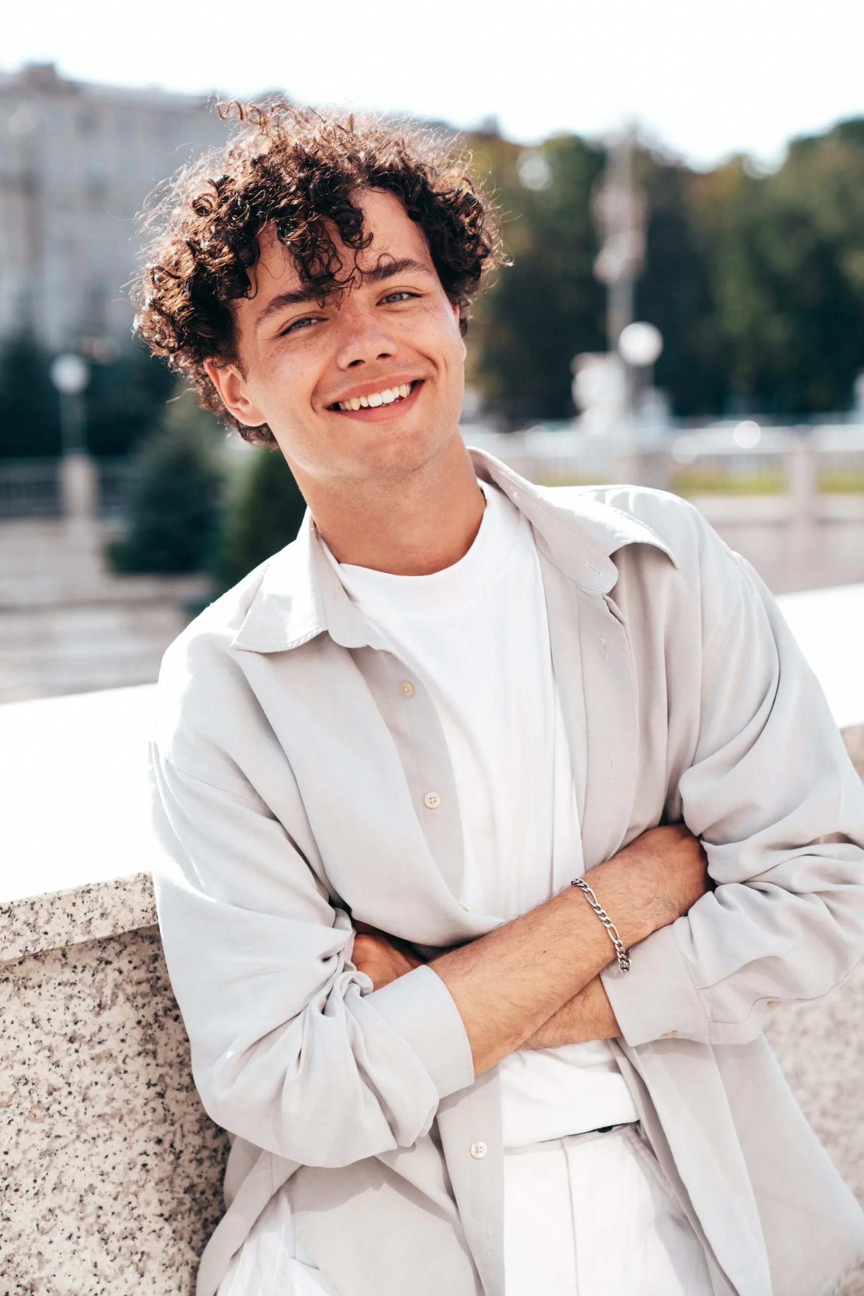 Smiling young man in beige shirt sitting outdoors in a park setting