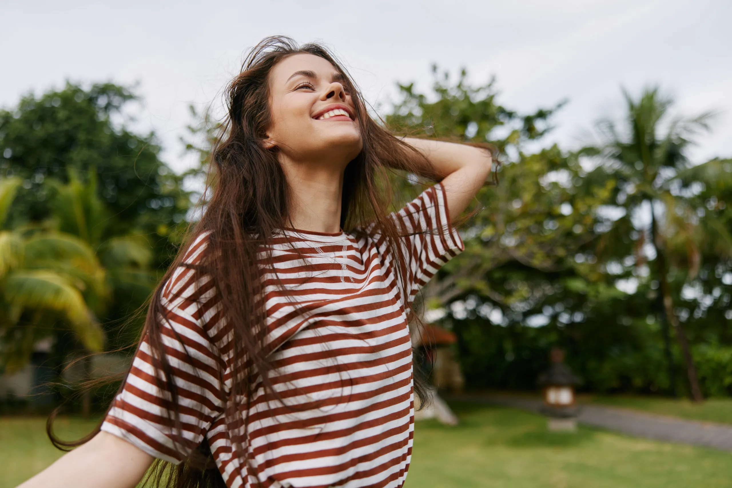 Woman in striped shirt smiling outdoors with tropical plants in background