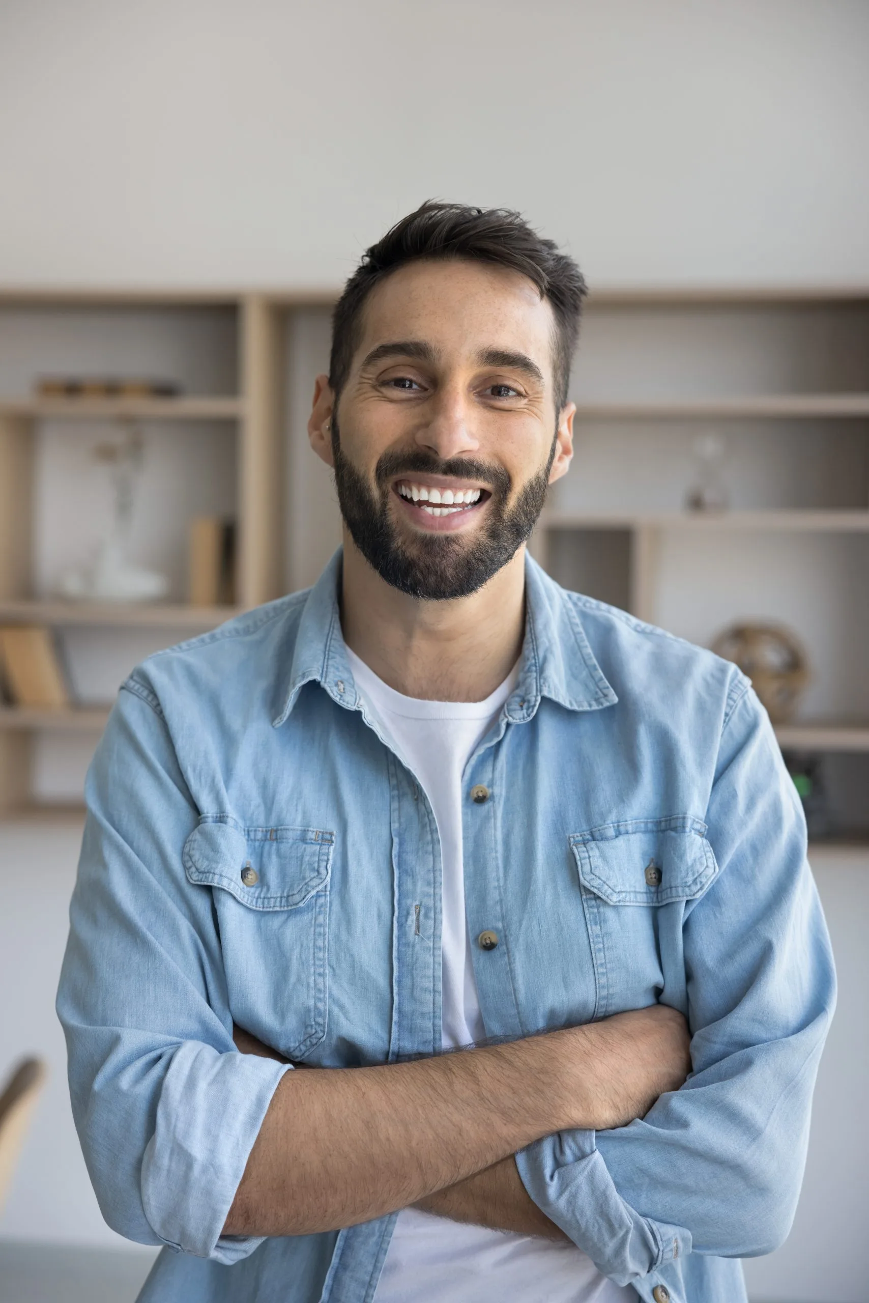 Man in denim shirt smiling at camera indoors with shelving behind him