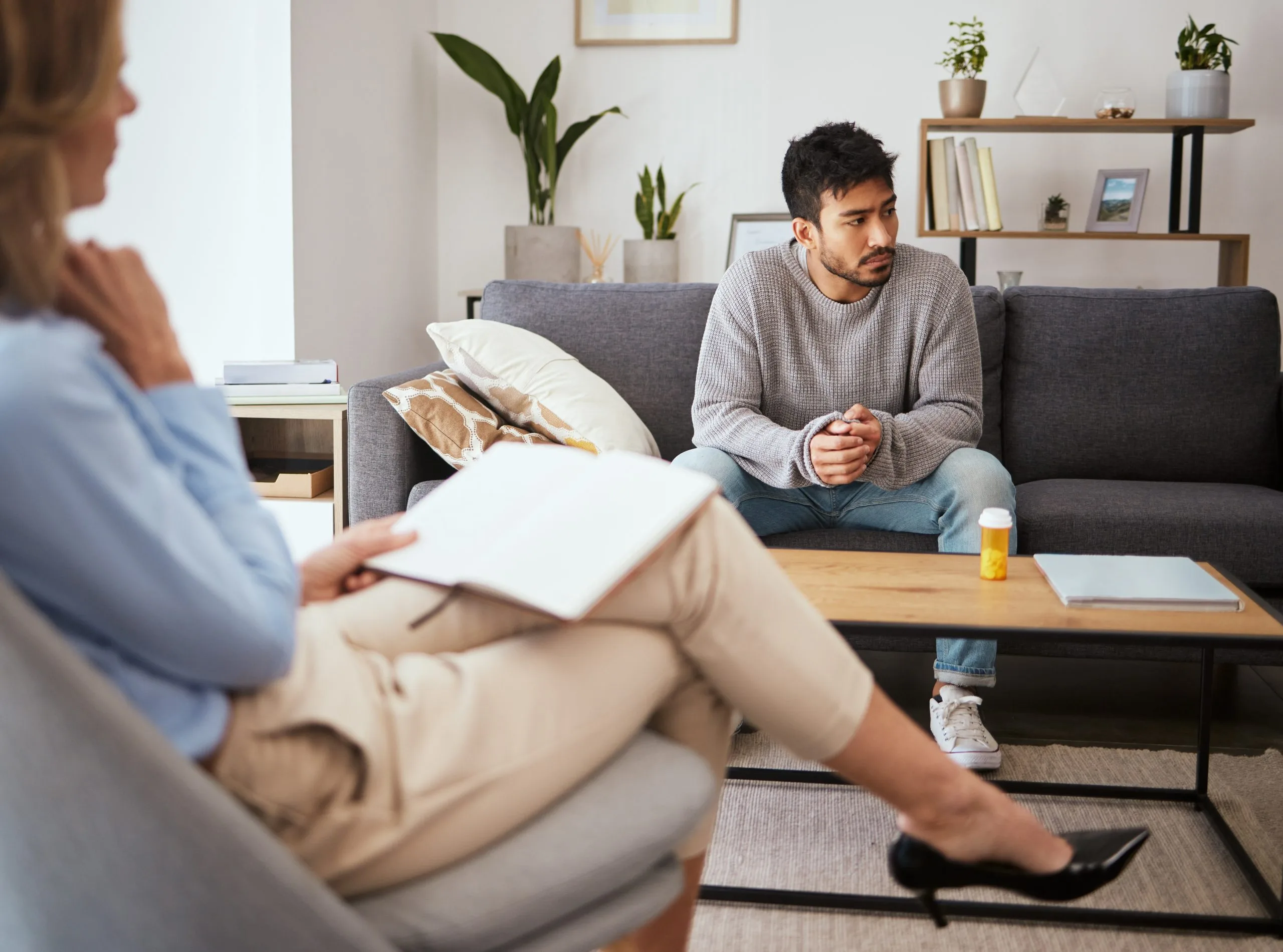 Therapist with clipboard listening to male patient during a mental health consultation in a comfortable office setting