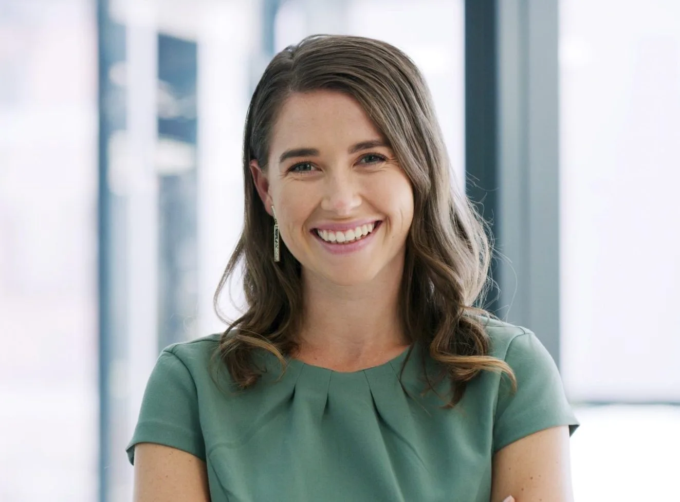 Woman smiling in bright office setting with blurred windows behind her