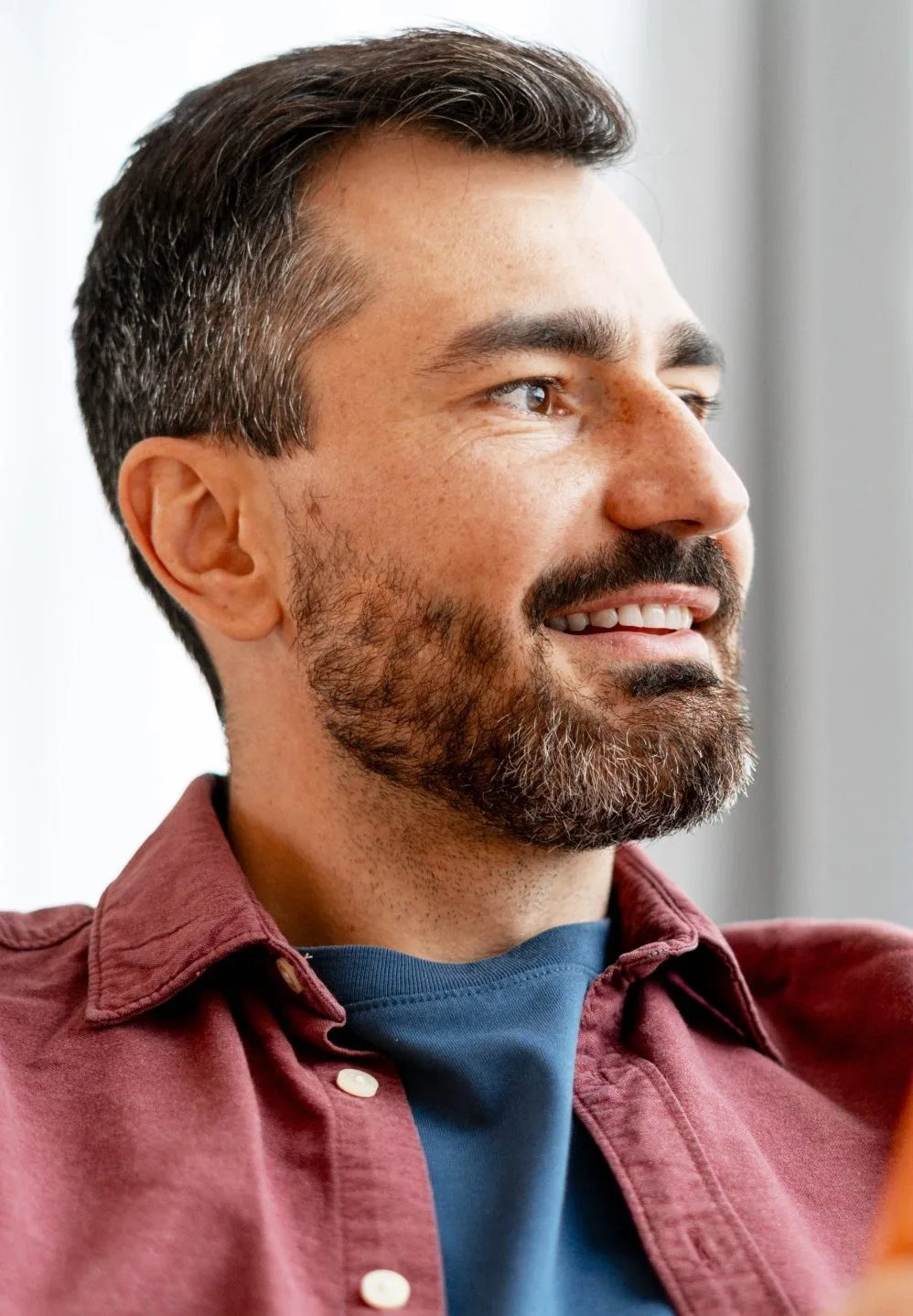 Man with beard smiling in profile wearing maroon and navy shirt
