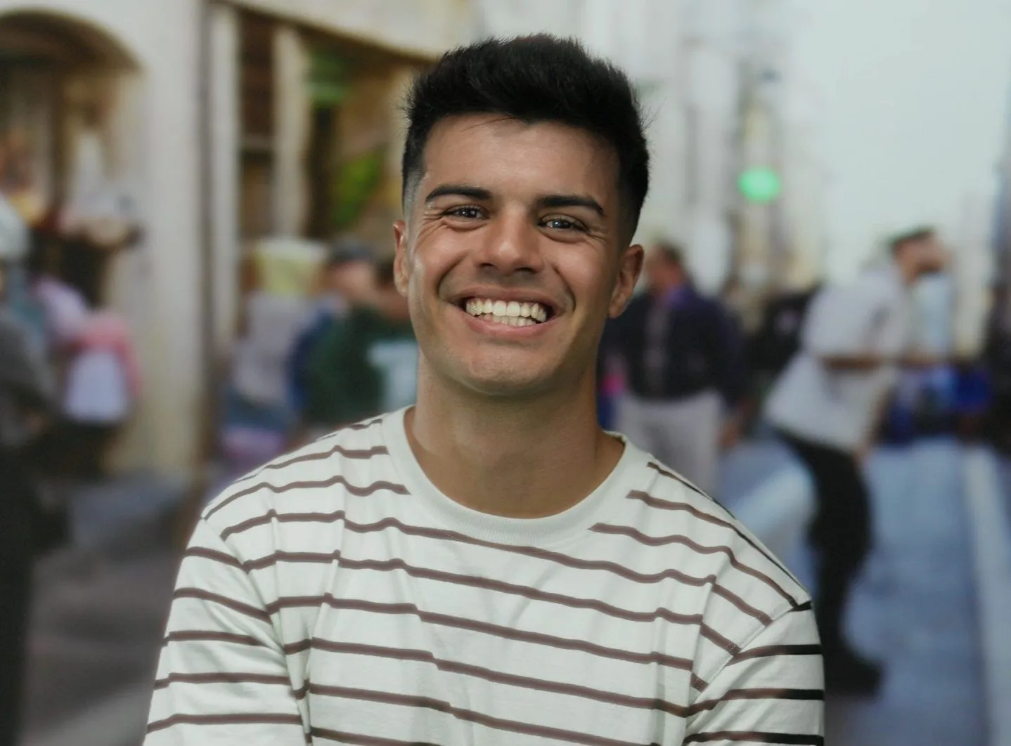 Young man smiling on a city street wearing a striped shirt