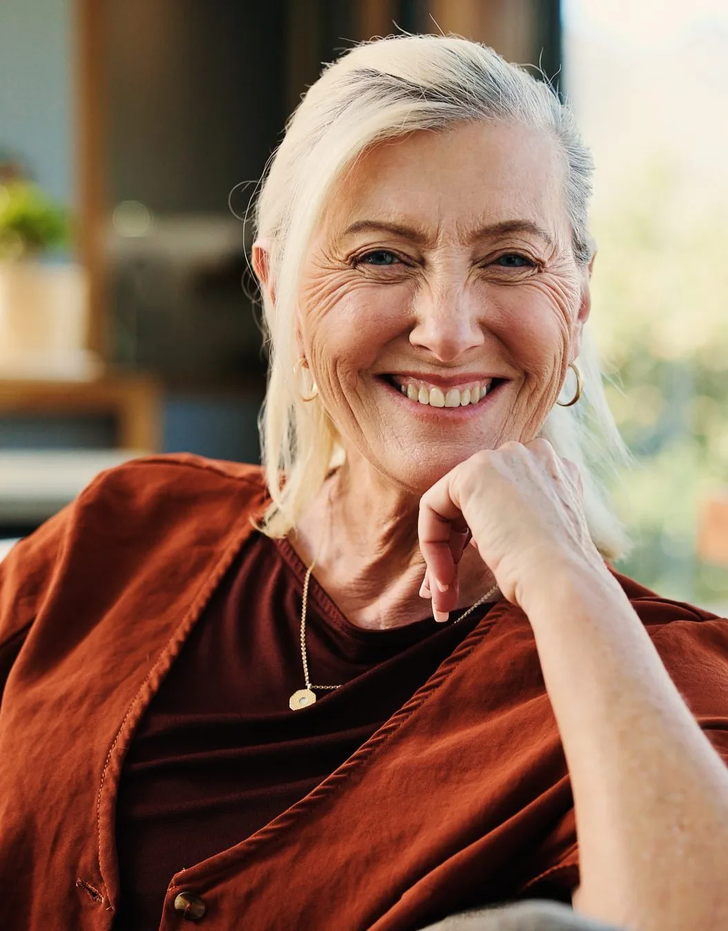 Stock photo of a smiling older woman with white hair wearing a rust-colored jacket