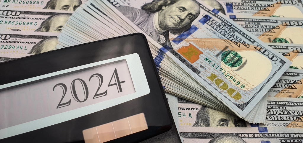 Calculator displaying 2024 next to fanned $100 bills, representing prevailing wage costs