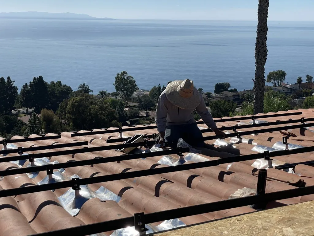 Worker installing clay roof tiles on commercial roofing with ocean coastline visible in background