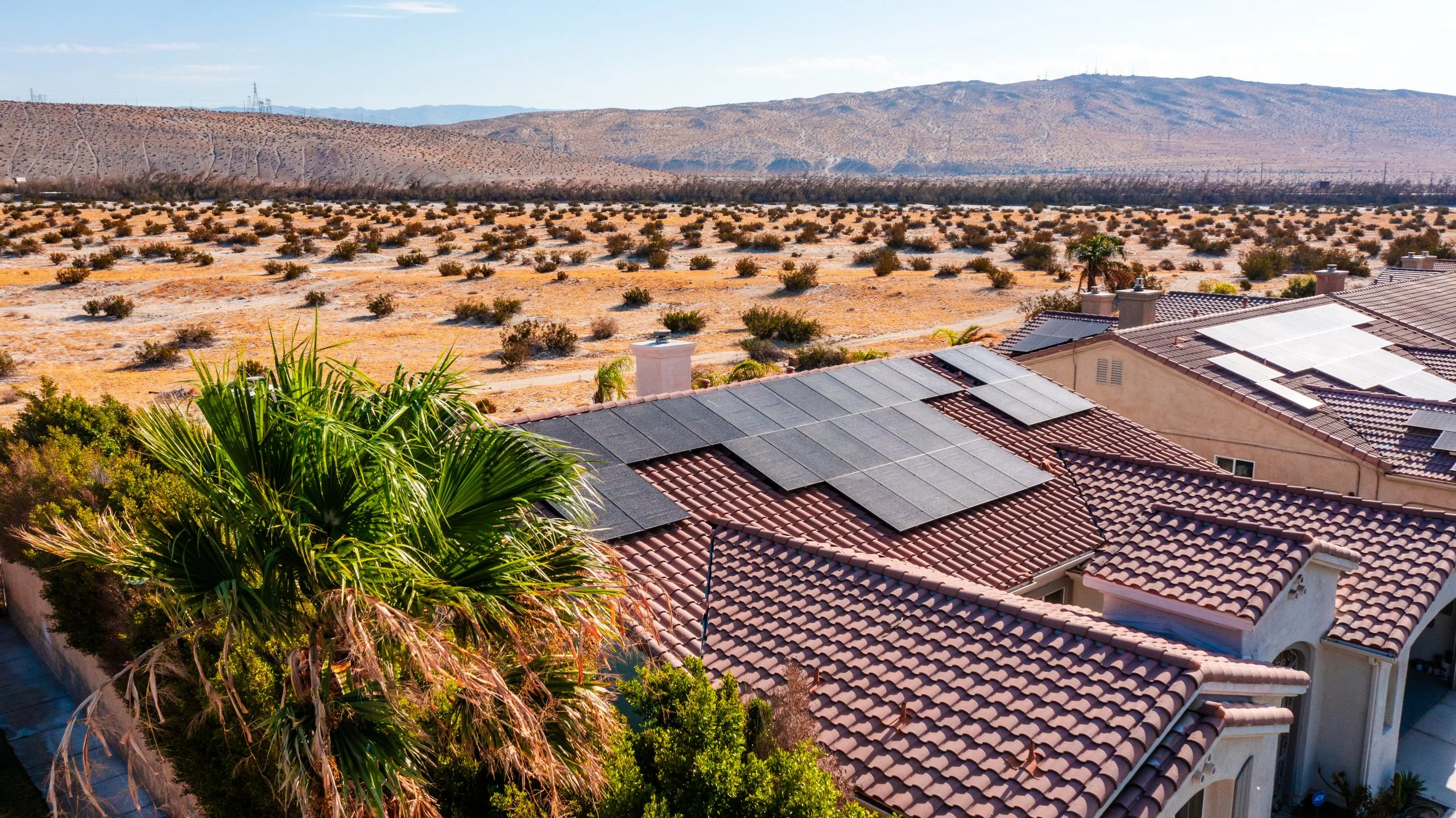 Aerial view of residential rooftop with solar panels overlooking desert landscape and mountains