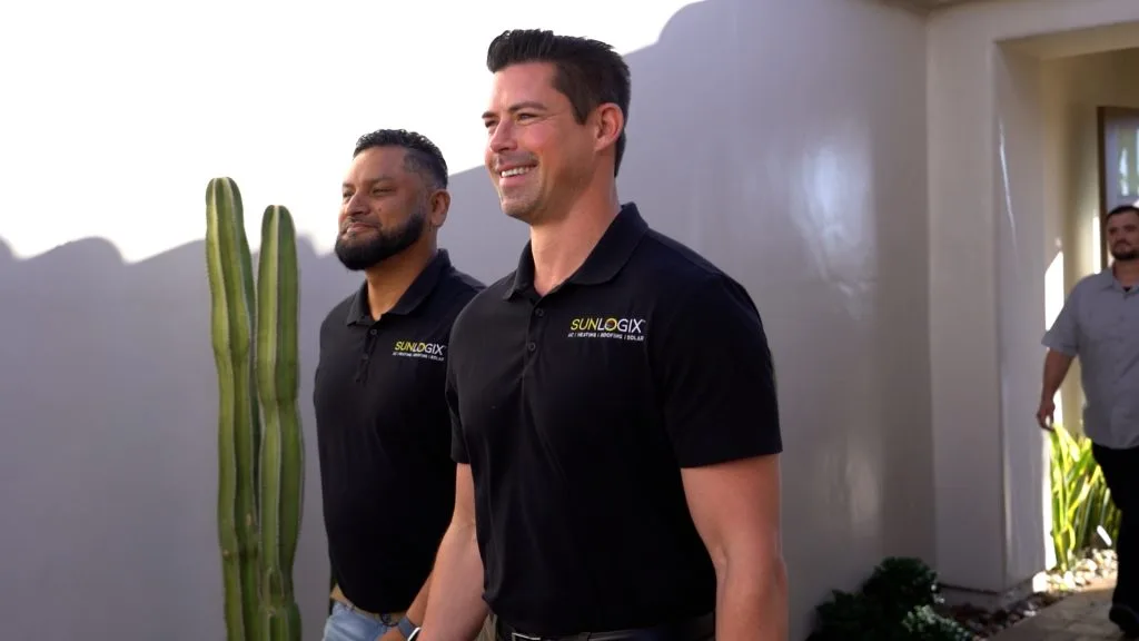 Two Sunlogix employees in black branded shirts standing in an entry hallway with a cactus plant