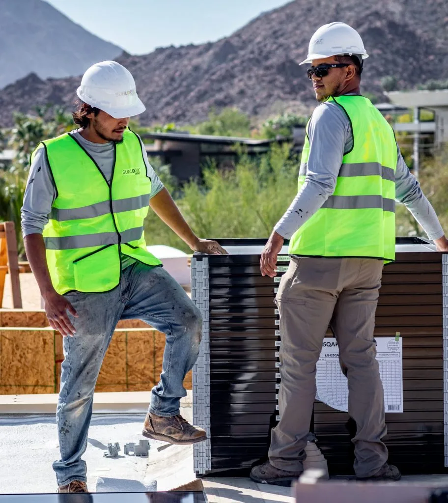 Two workers in safety vests and hard hats inspecting HVAC equipment on rooftop