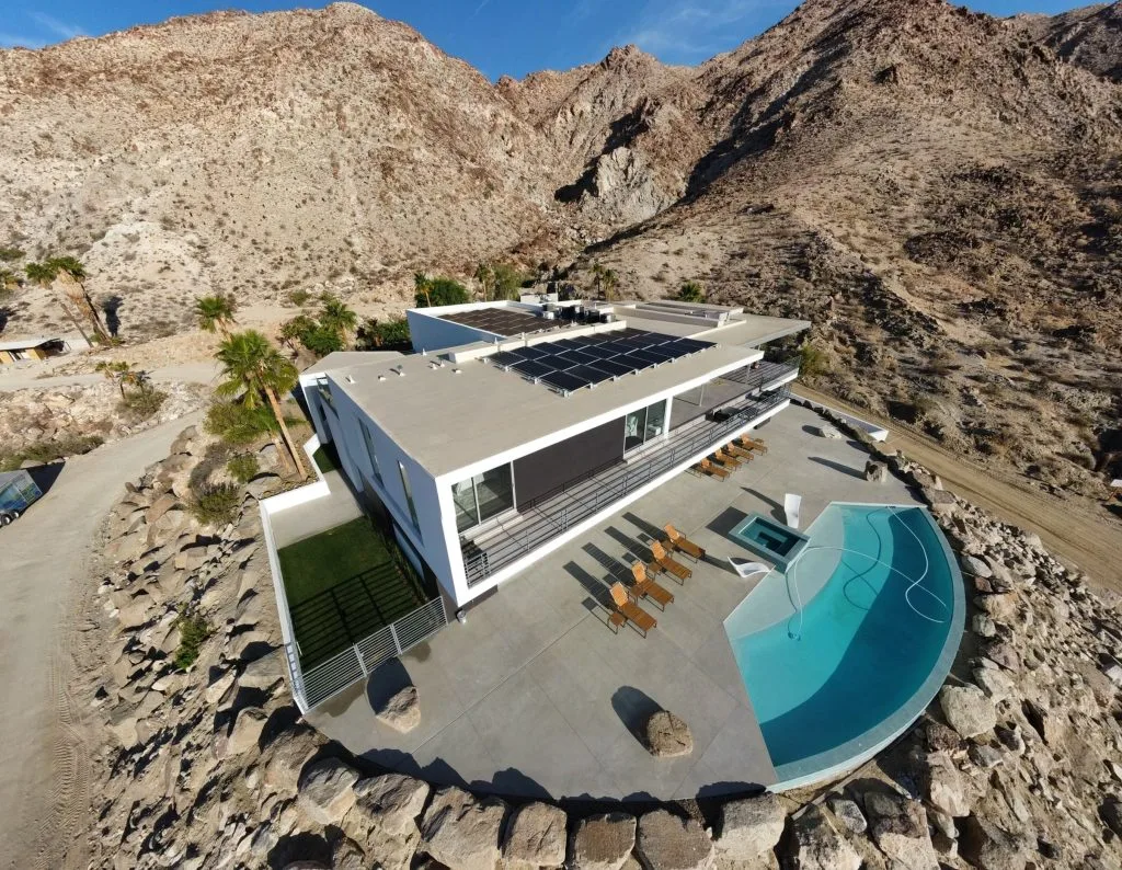 Modern white building with solar panels on roof nestled in desert canyon with turquoise pool in foreground