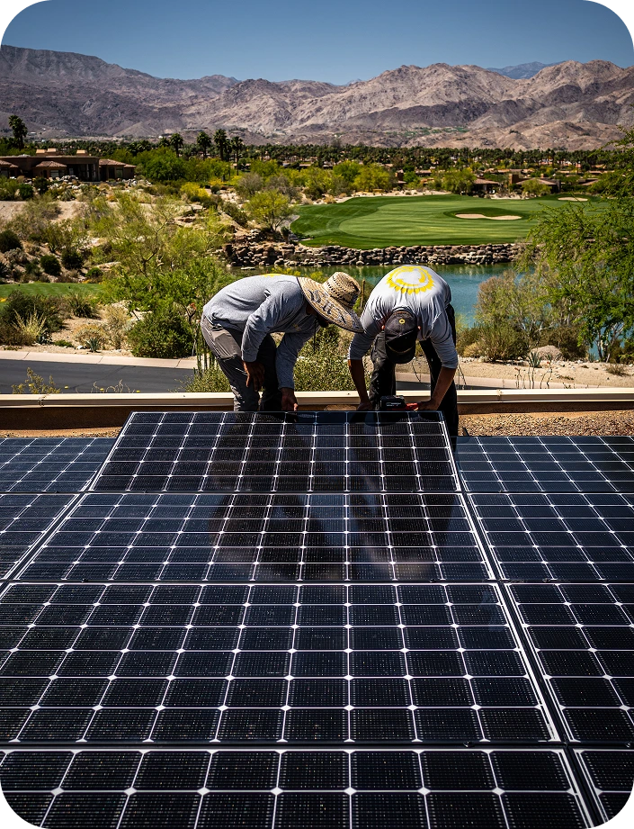 Two solar technicians installing solar panels on a rooftop overlooking a desert valley with mountains and green vegetation