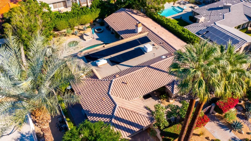 Aerial view of multiple residential roofs with installed solar panel systems and palm trees
