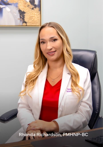 Rhonda Richardson, PMHNP-BC, psychiatric mental health nurse practitioner, seated at desk wearing white coat and red top