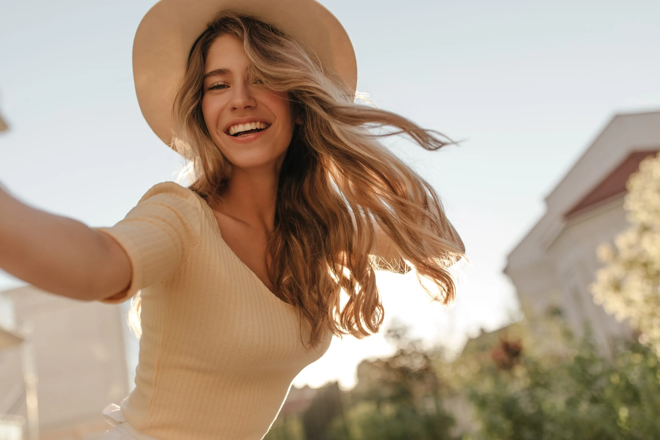 Woman smiling outdoors wearing a tan hat and light-colored top