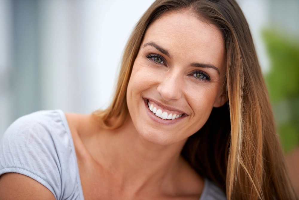 Smiling woman with shoulder-length reddish-brown hair wearing a light blue shirt outdoors