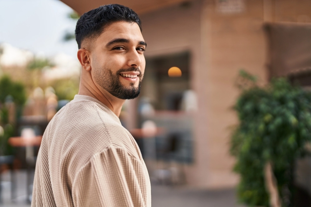 Smiling man in beige shirt standing outdoors in front of a residential building