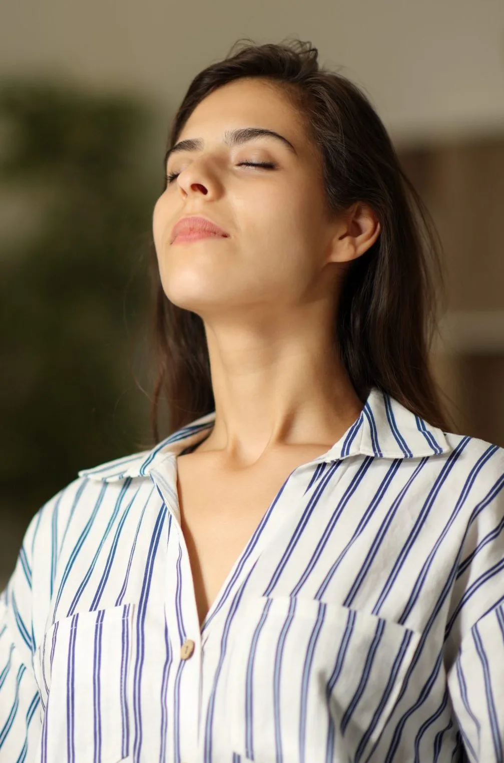 Woman with eyes closed wearing blue-striped shirt, appearing calm and peaceful