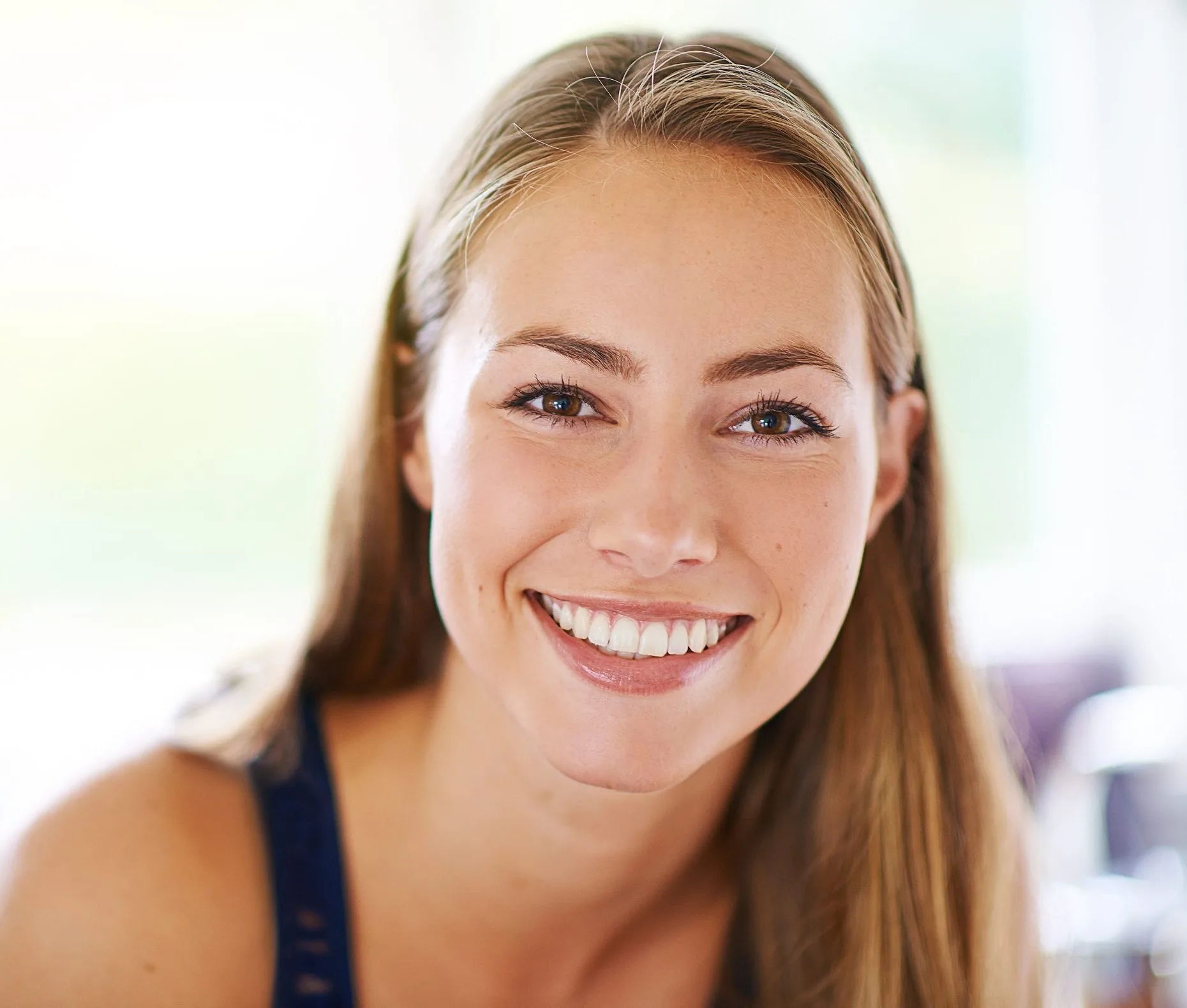 Woman with long brown hair smiling at camera in bright indoor setting