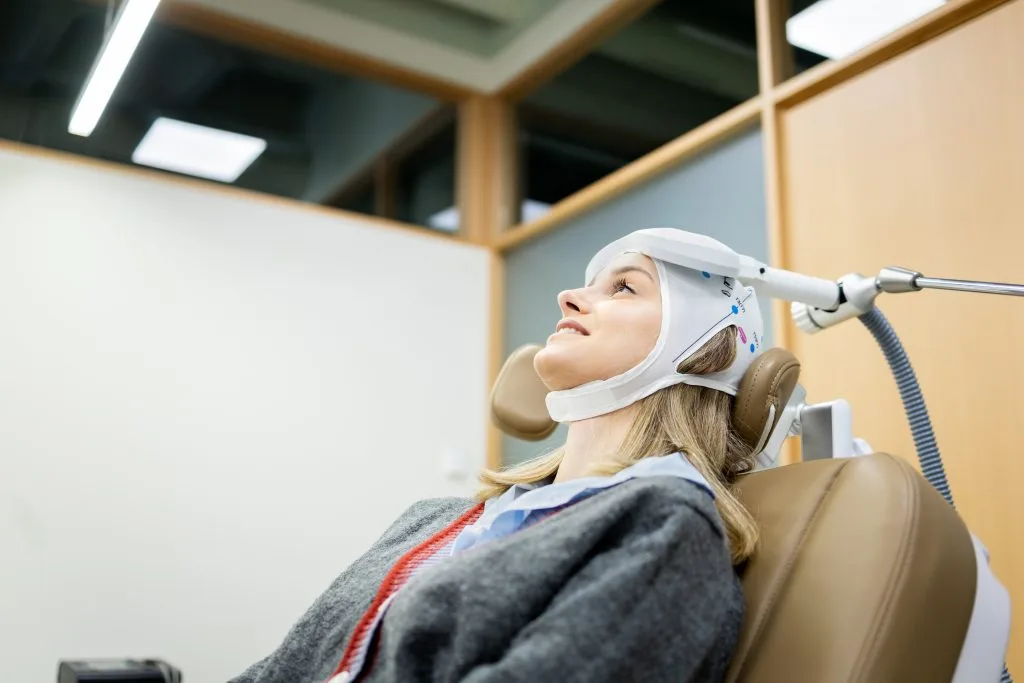 Patient in white head brace tilted back in dental chair during procedure with overhead light
