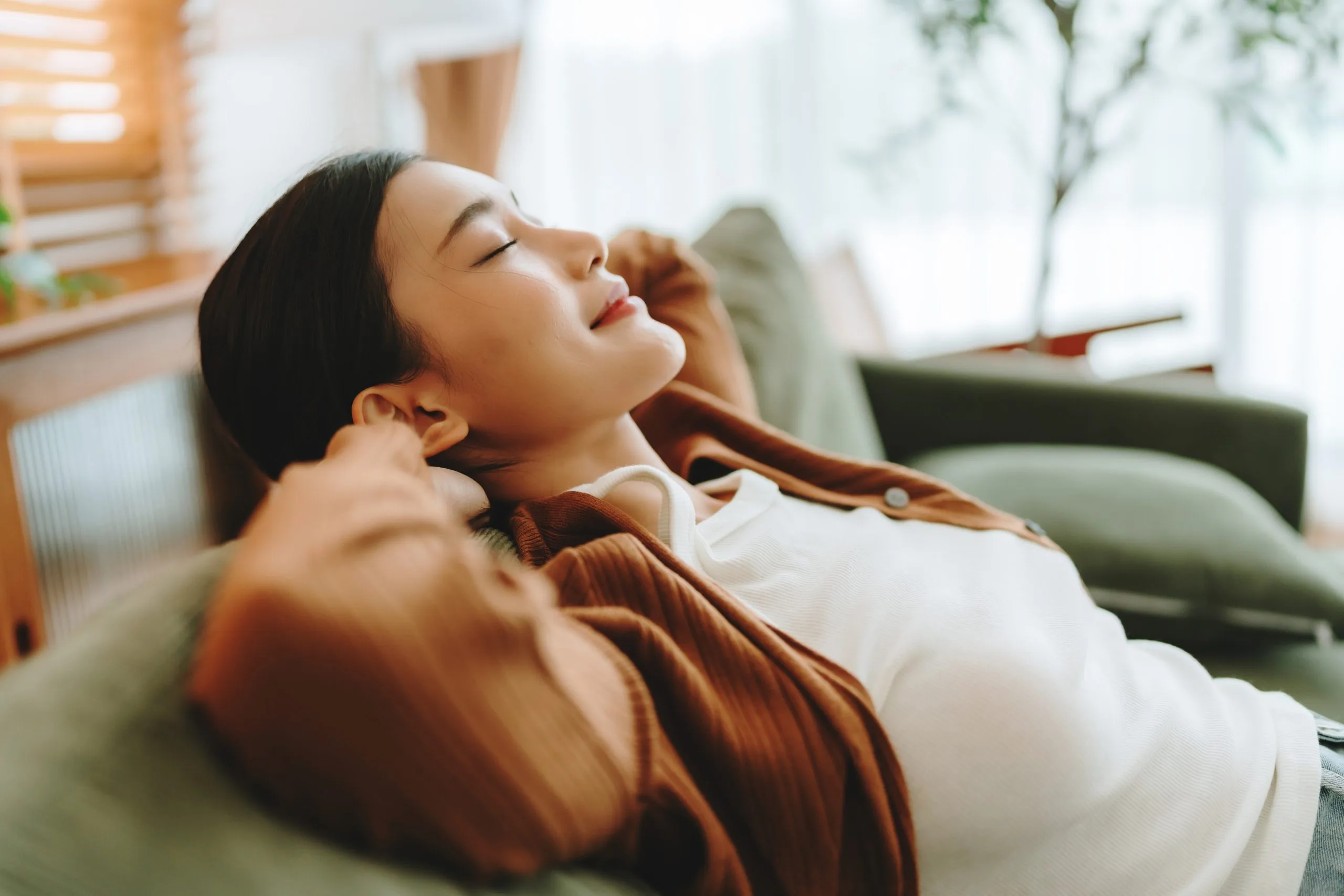 Woman relaxing on green chair in bright room with eyes closed