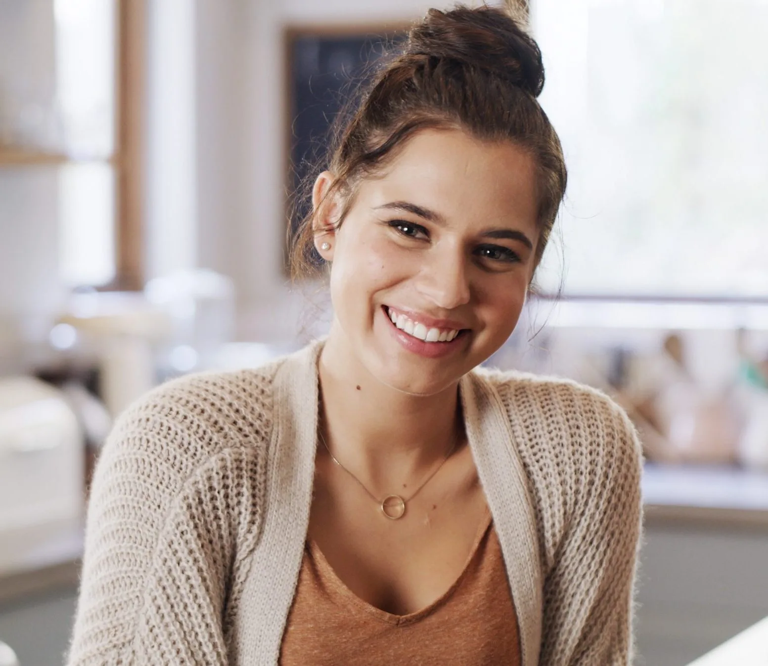 Young woman smiling indoors wearing a beige cardigan in a bright kitchen