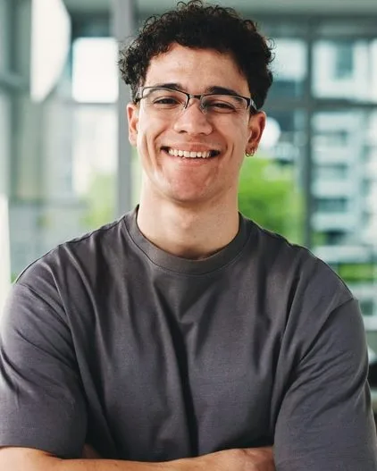 Young man smiling at camera indoors wearing glasses and a dark t-shirt