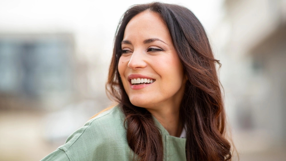 Woman smiling outdoors in green shirt against blurred urban background