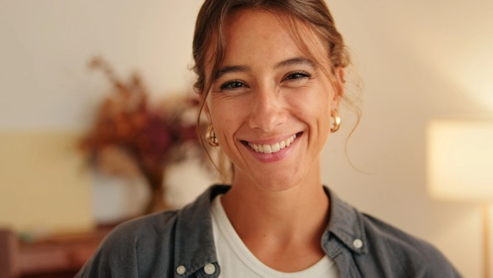 Woman smiling at camera indoors wearing a dark button-up shirt