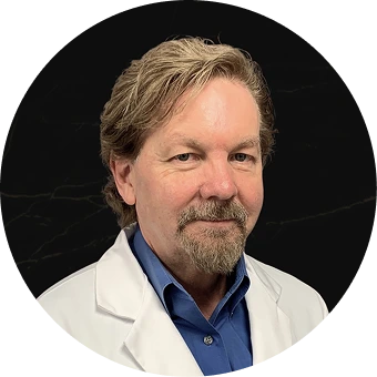 Male physician in white coat and blue shirt against black background