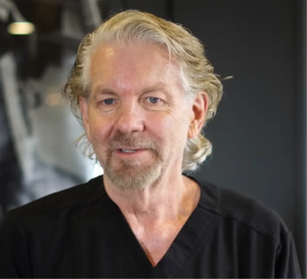 Male practitioner with blonde hair in black v-neck shirt in clinical setting