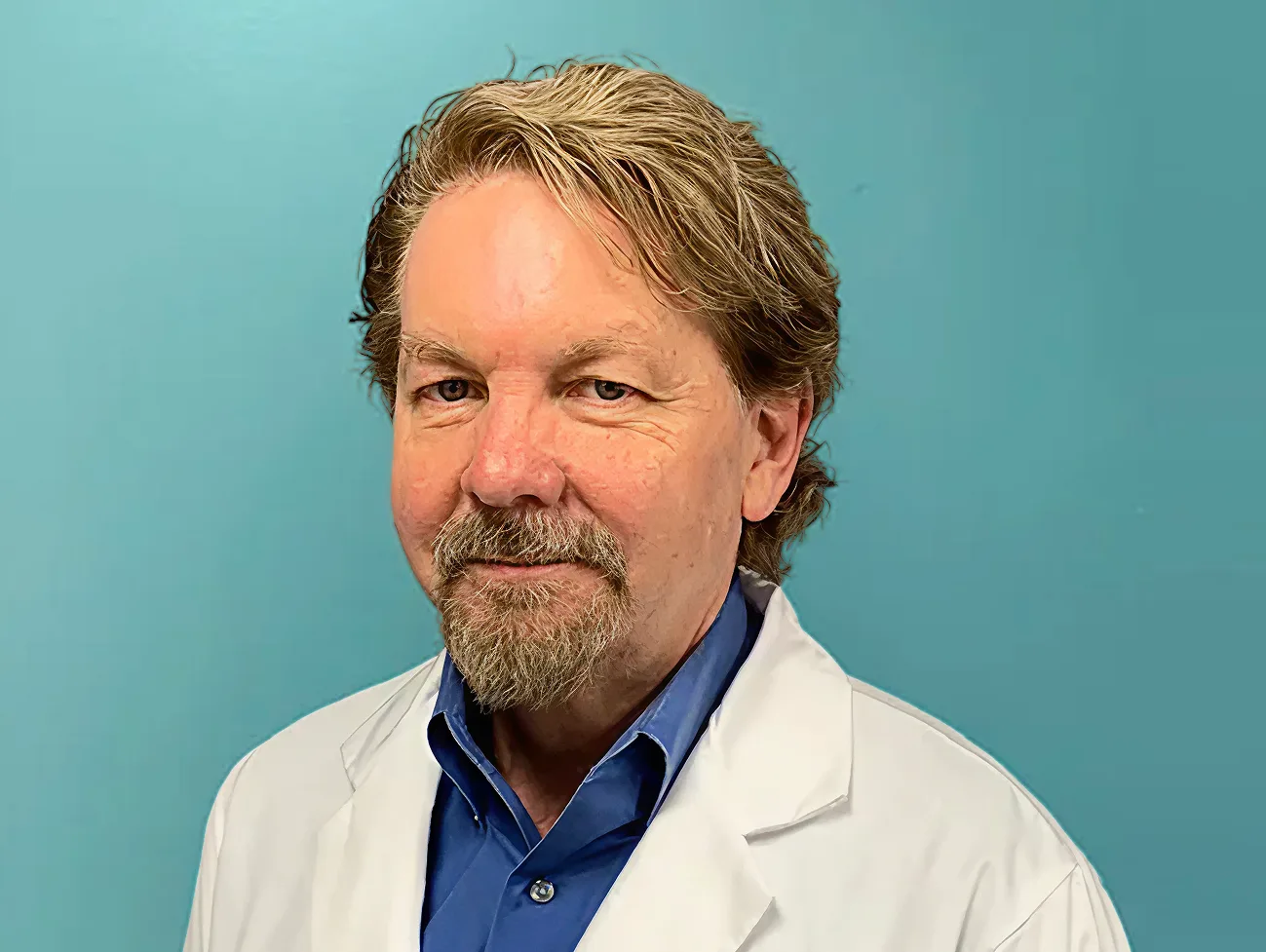 Male healthcare provider wearing white lab coat over blue shirt against teal background