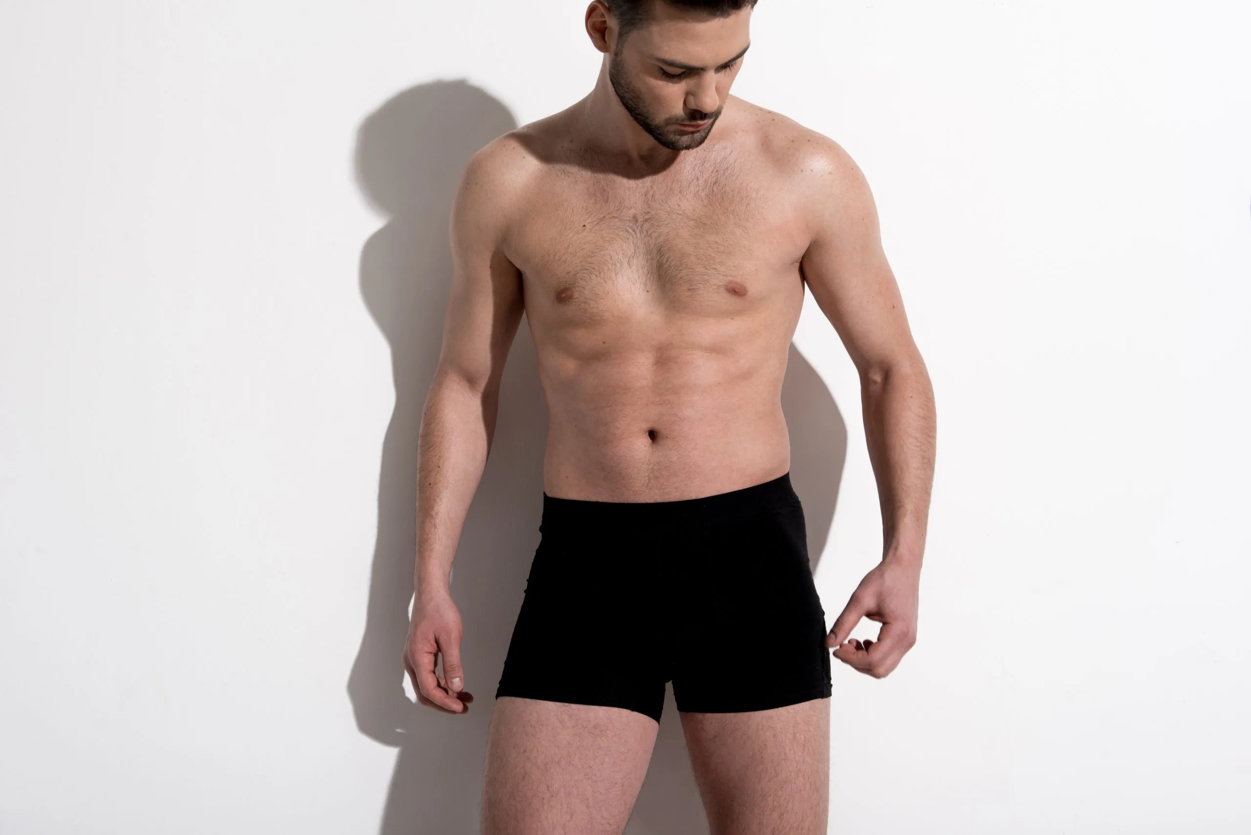 Man in black boxer shorts looking down against white background