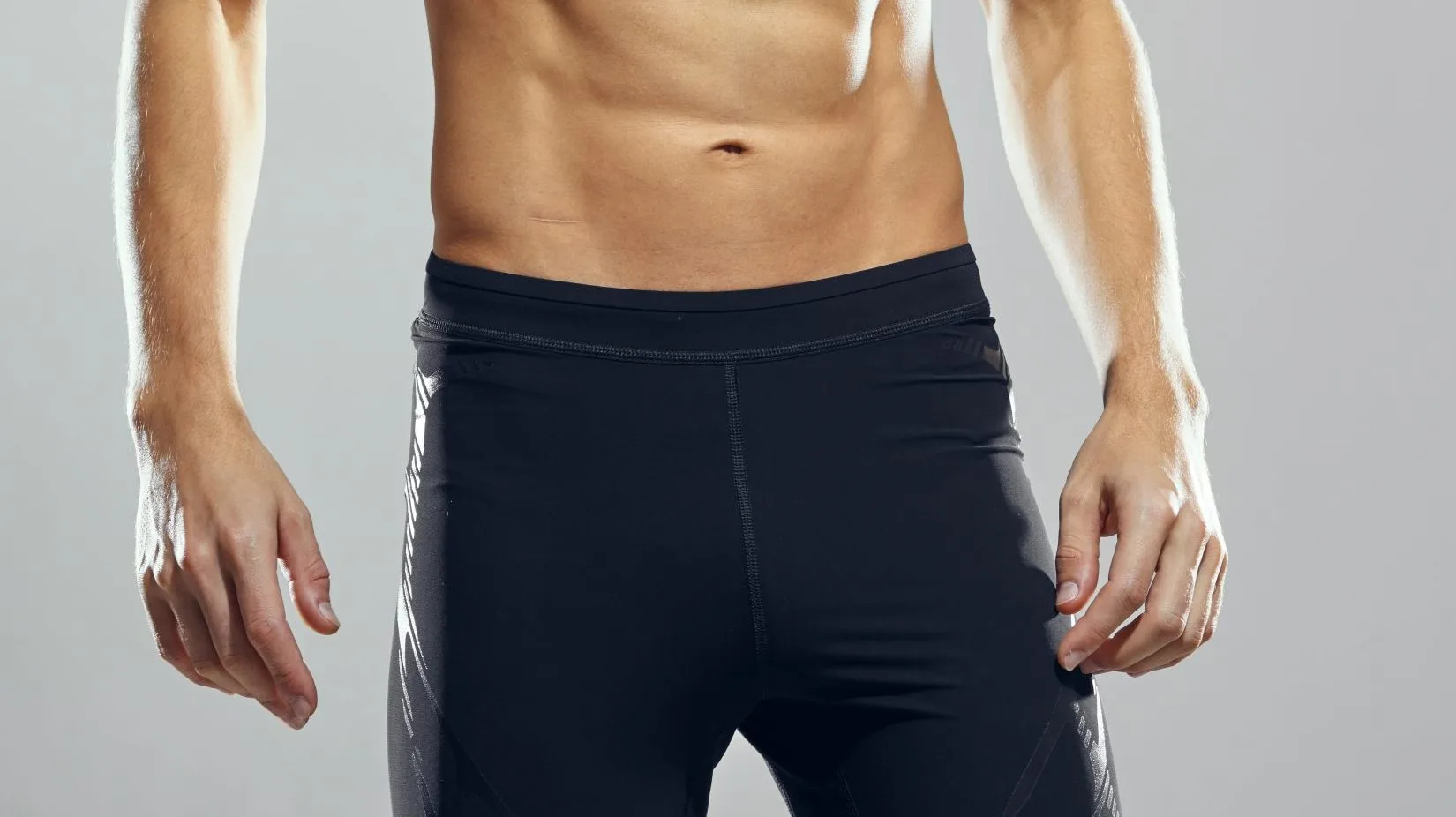 Man's torso and lower body wearing dark navy athletic shorts against gray background
