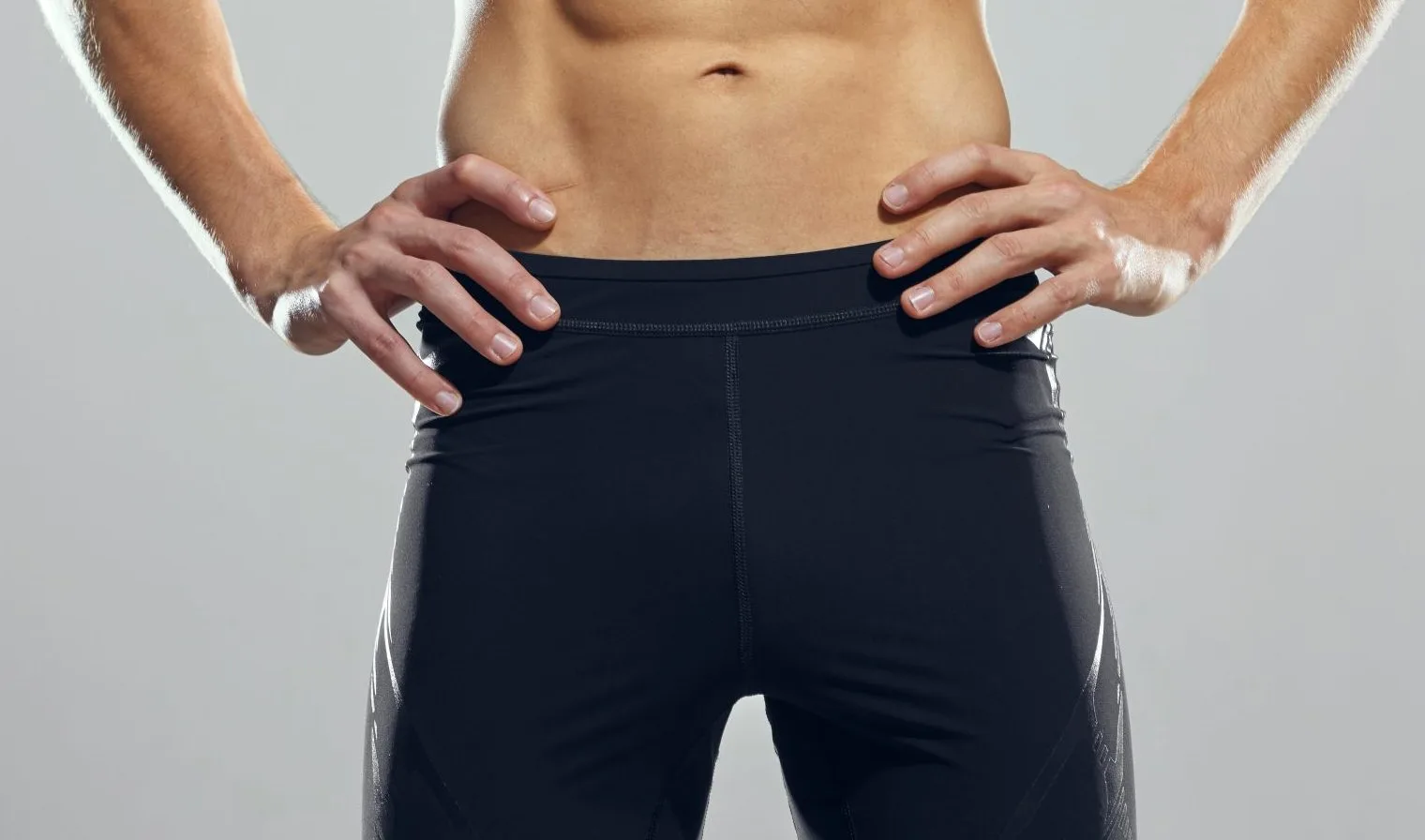 Man with hands on hips wearing dark navy athletic shorts against gray background