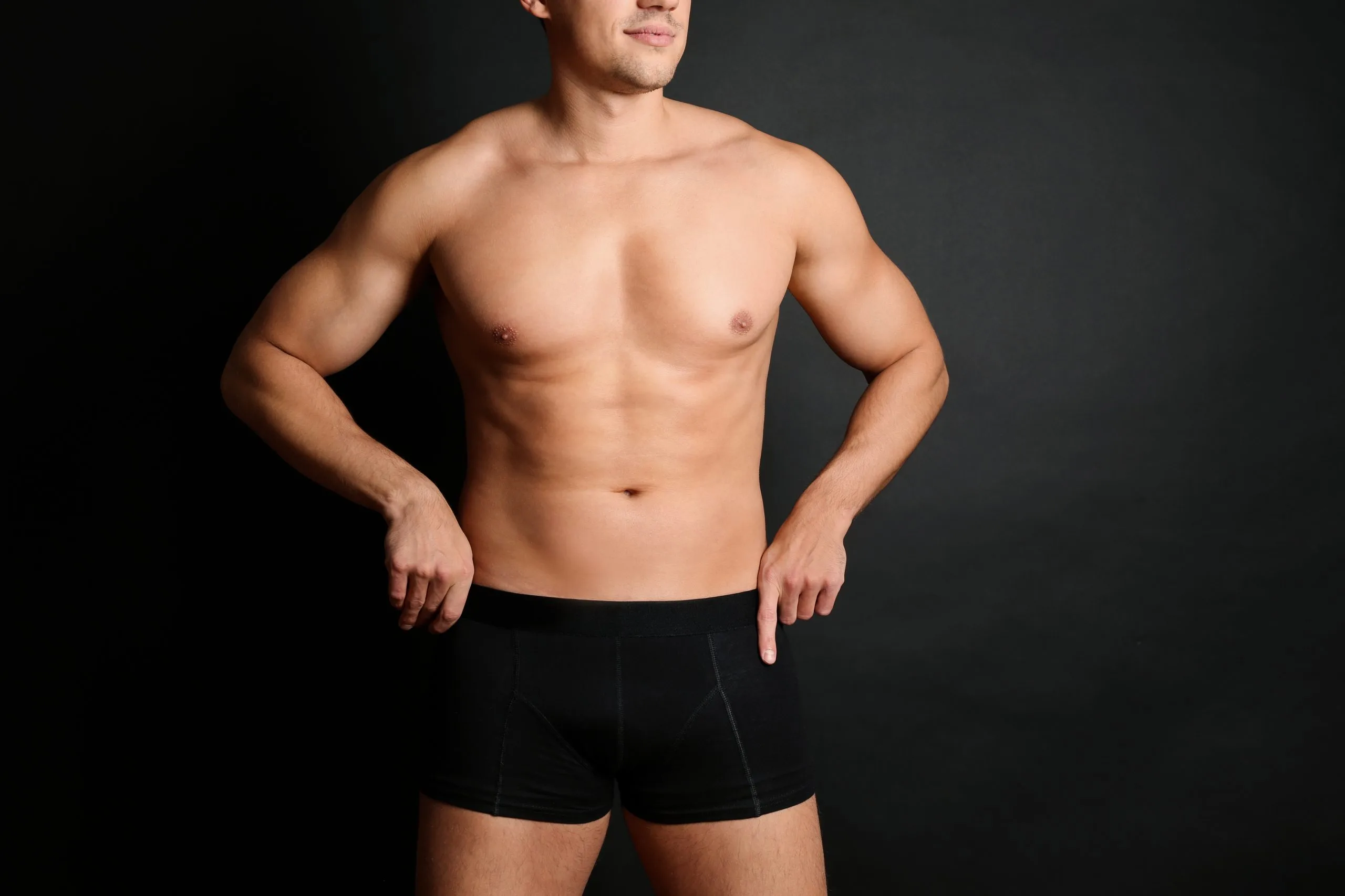 Shirtless man with muscular build standing against black background