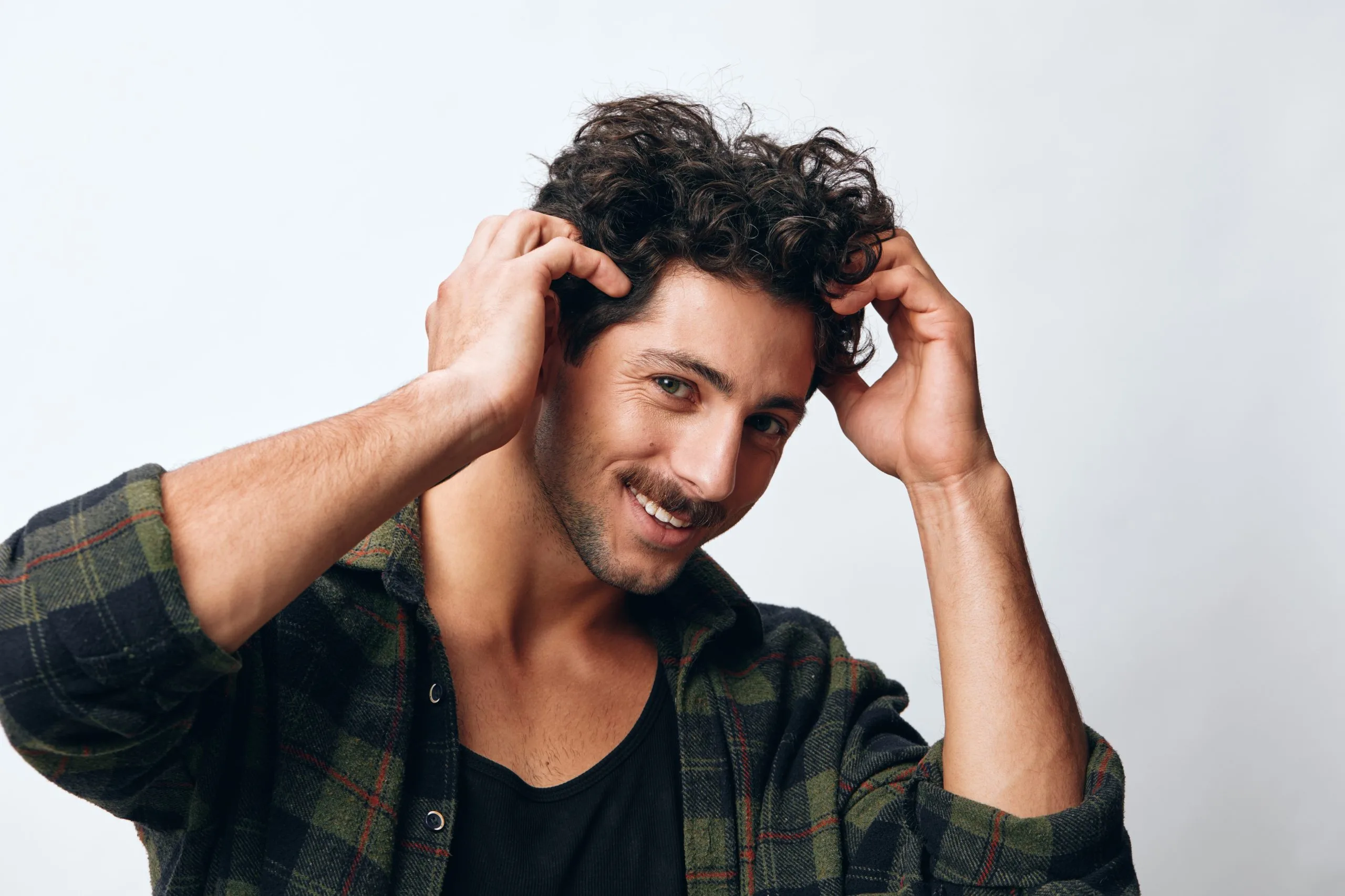 Man in plaid shirt smiling while running hands through his dark curly hair