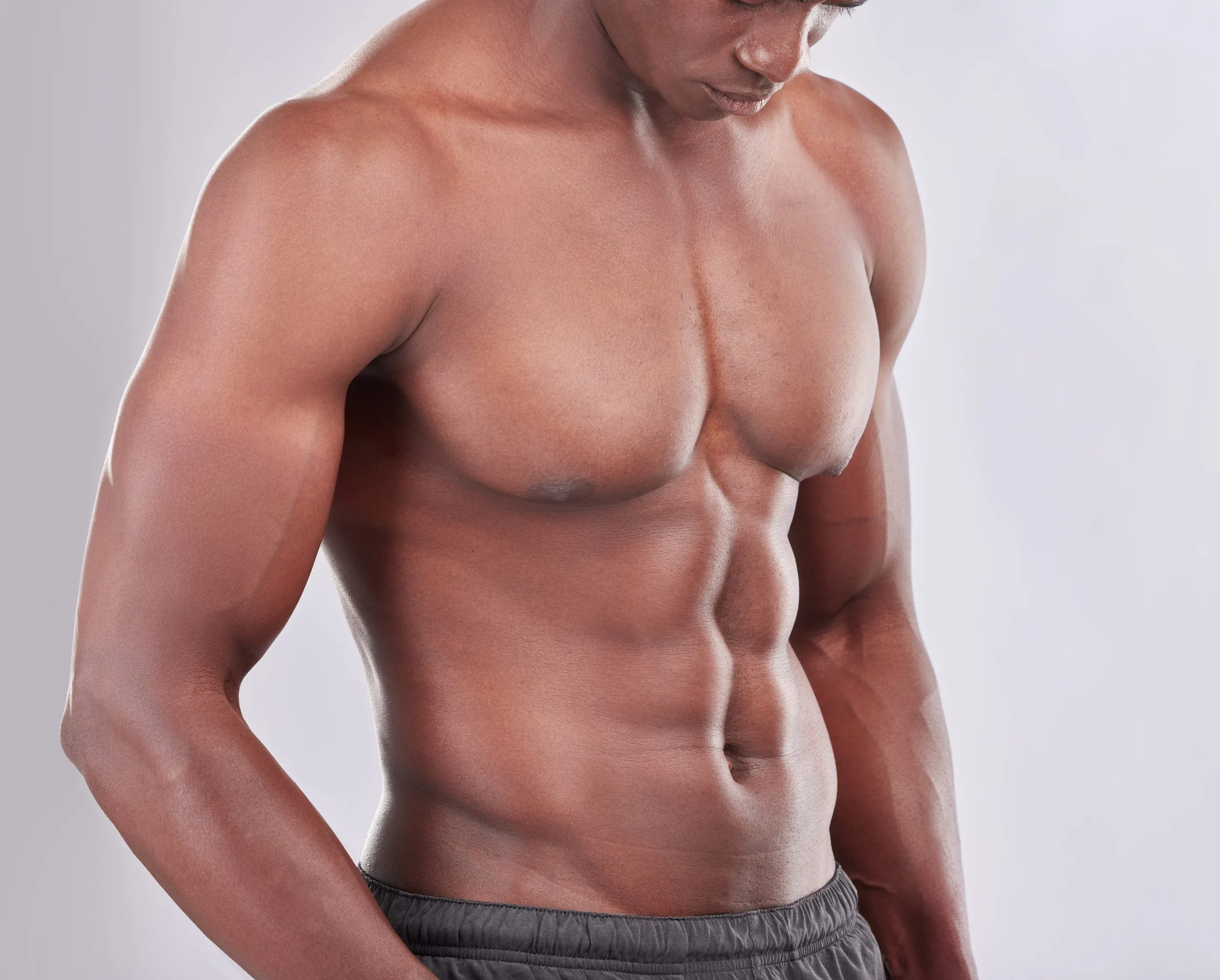 Shirtless man with defined abdominal muscles looking downward against gray background