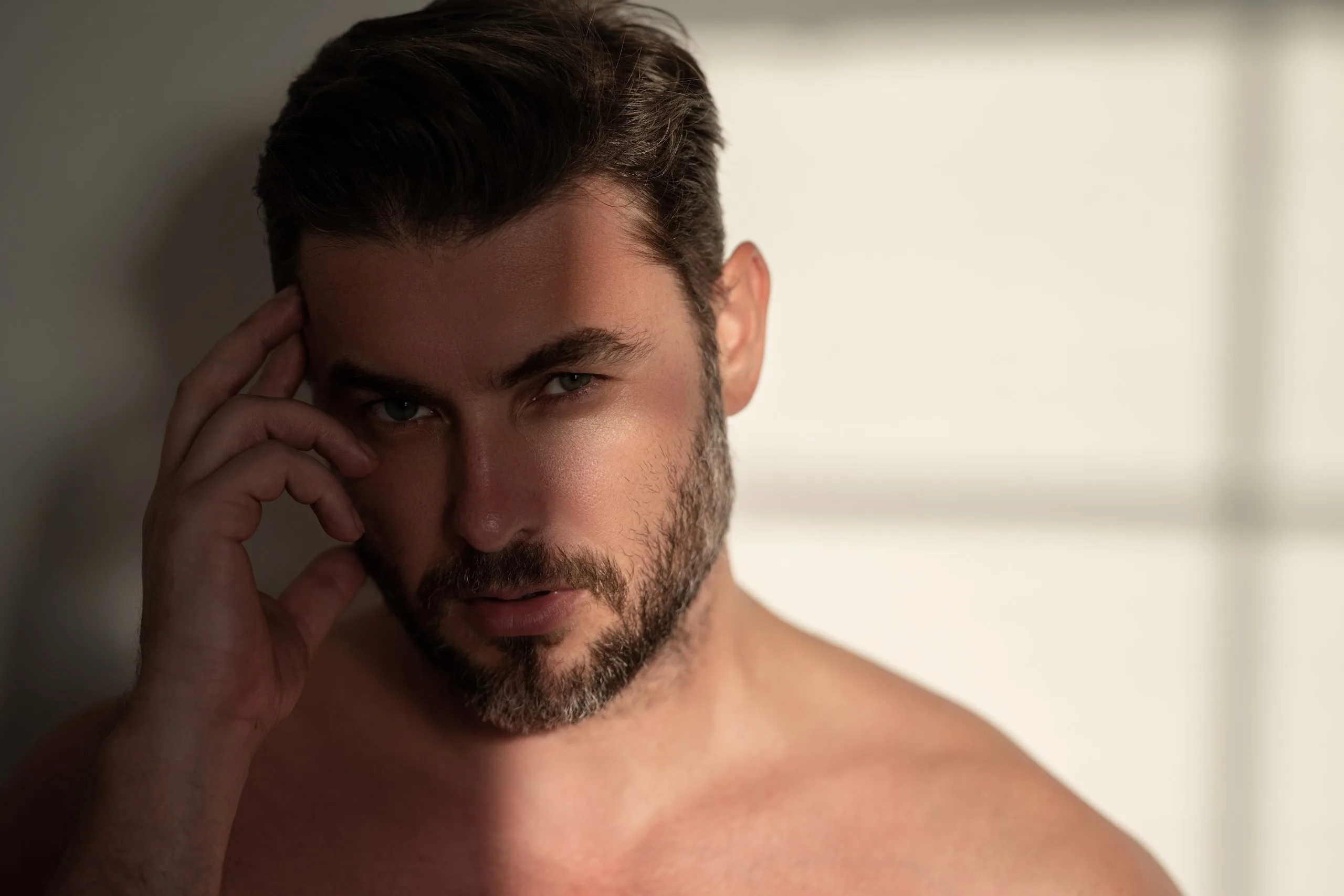 Man with dark hair and beard touching his face with contemplative expression