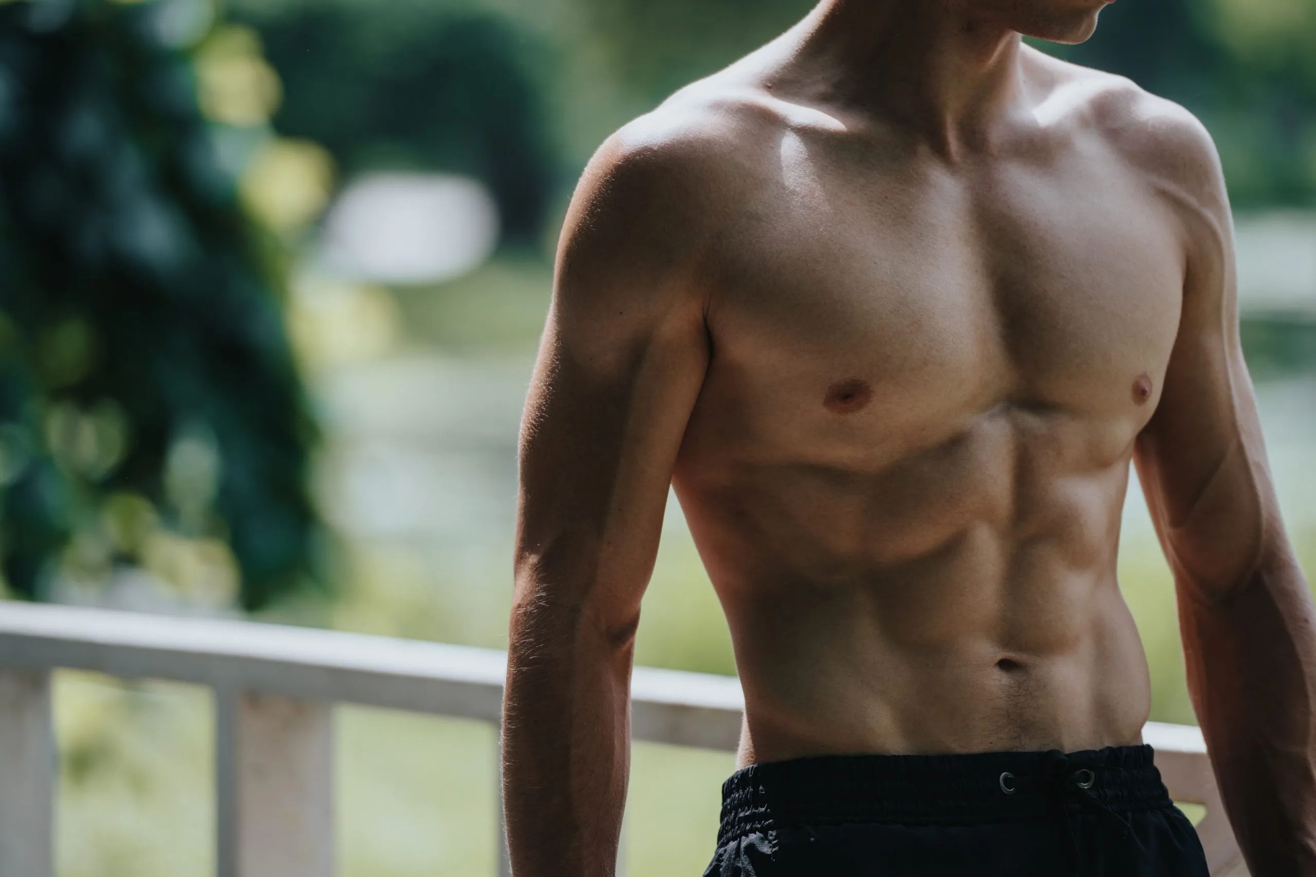 Shirtless man standing outdoors with blurred garden background