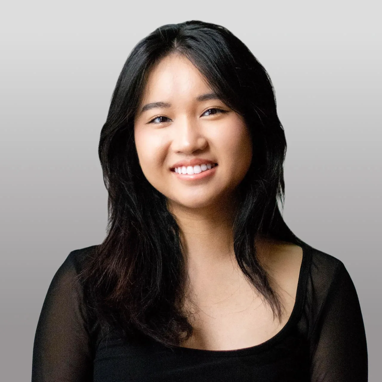 Woman with long black hair smiling at camera against gray background