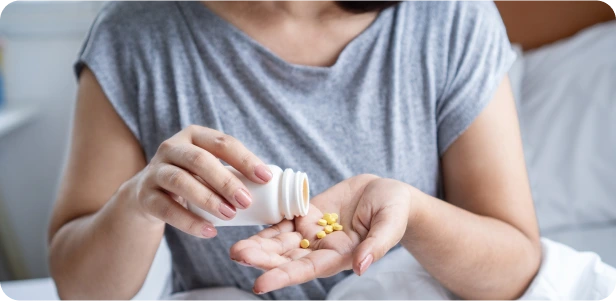 Person holding and pouring yellow pills into their palm from a white bottle