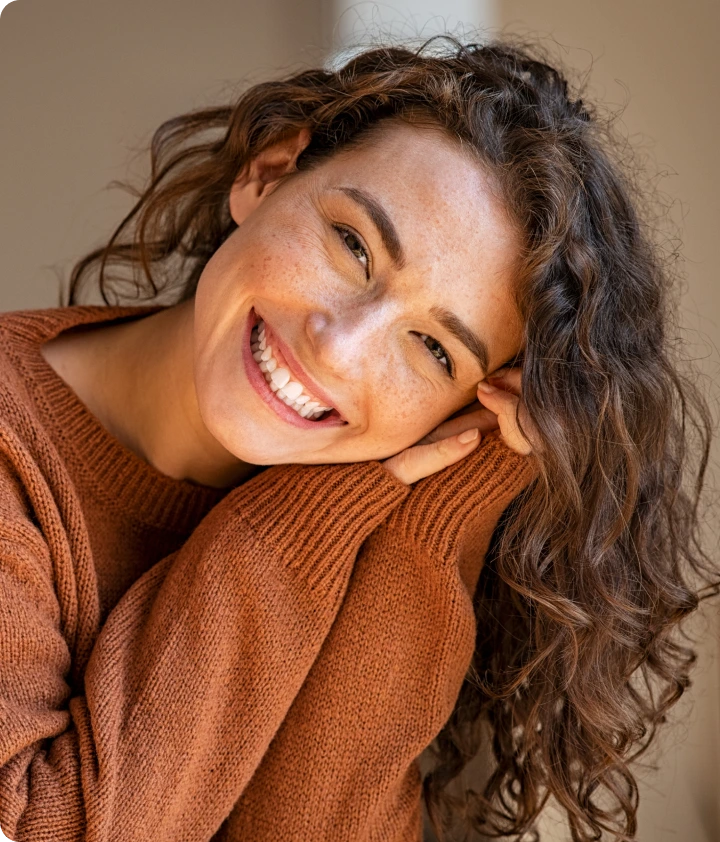 Woman smiling warmly at camera while hugging herself in a rust-colored sweater