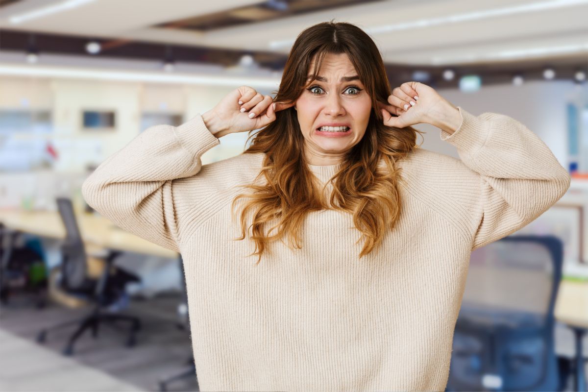 Woman in office covering her ears with an overwhelmed expression, depicting sensory sensitivity